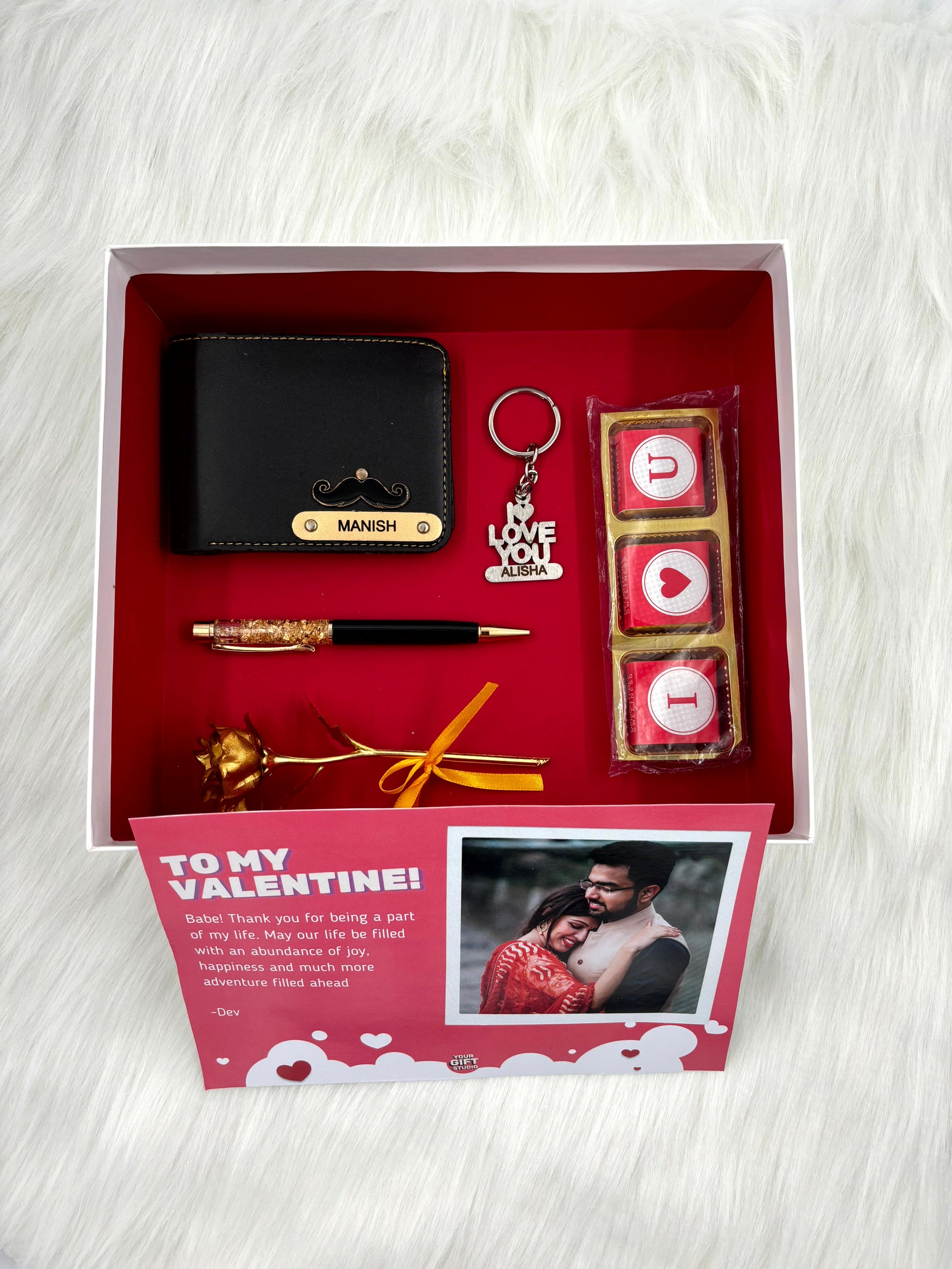 A top view of a box containing customized leather wallet, I Love You chocolate & keychain, gold flaked pen along with a gold rose.