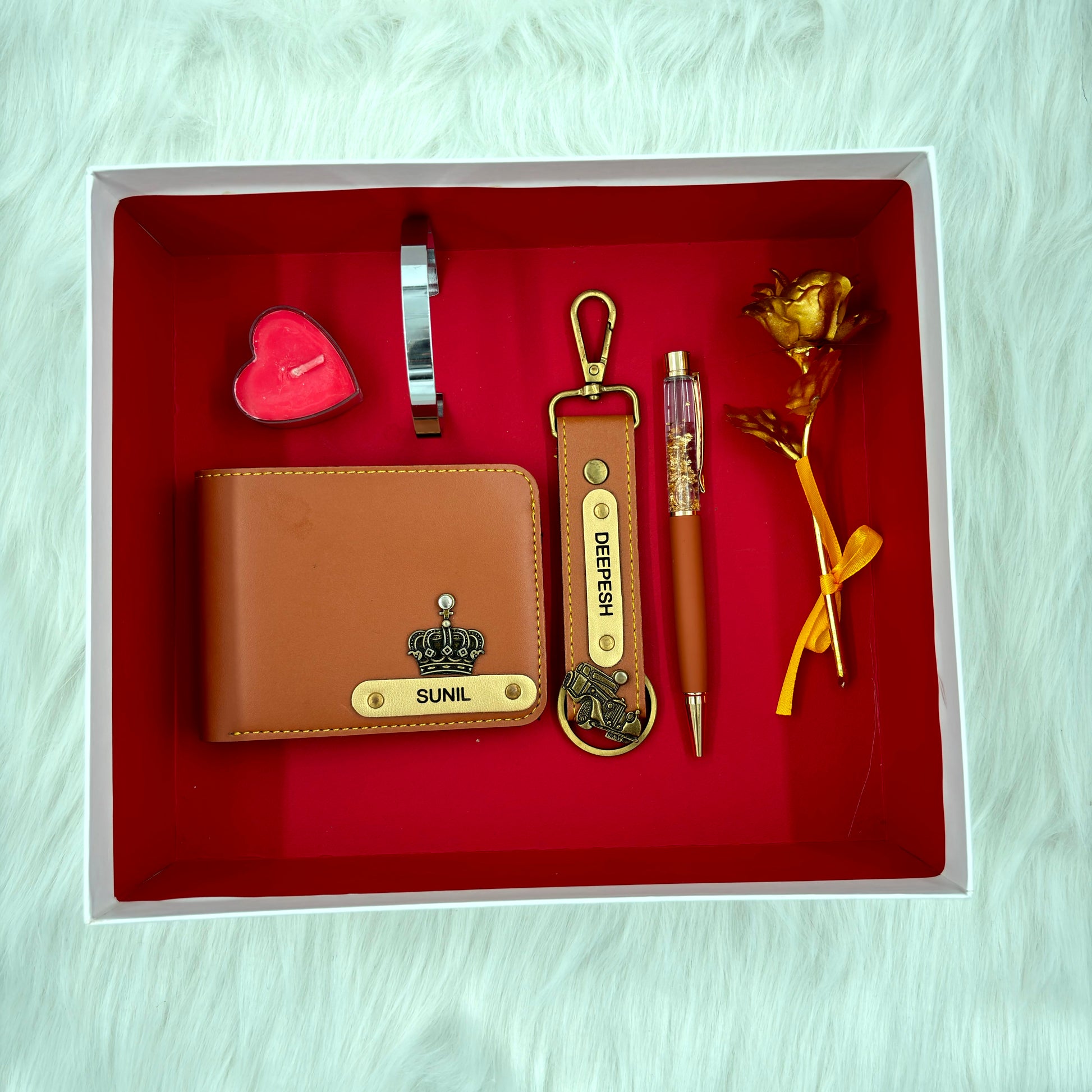A top view of a box containing customized tan leather wallet, keychain, gold flake pen, kada, scented candle and gold plated rose.
