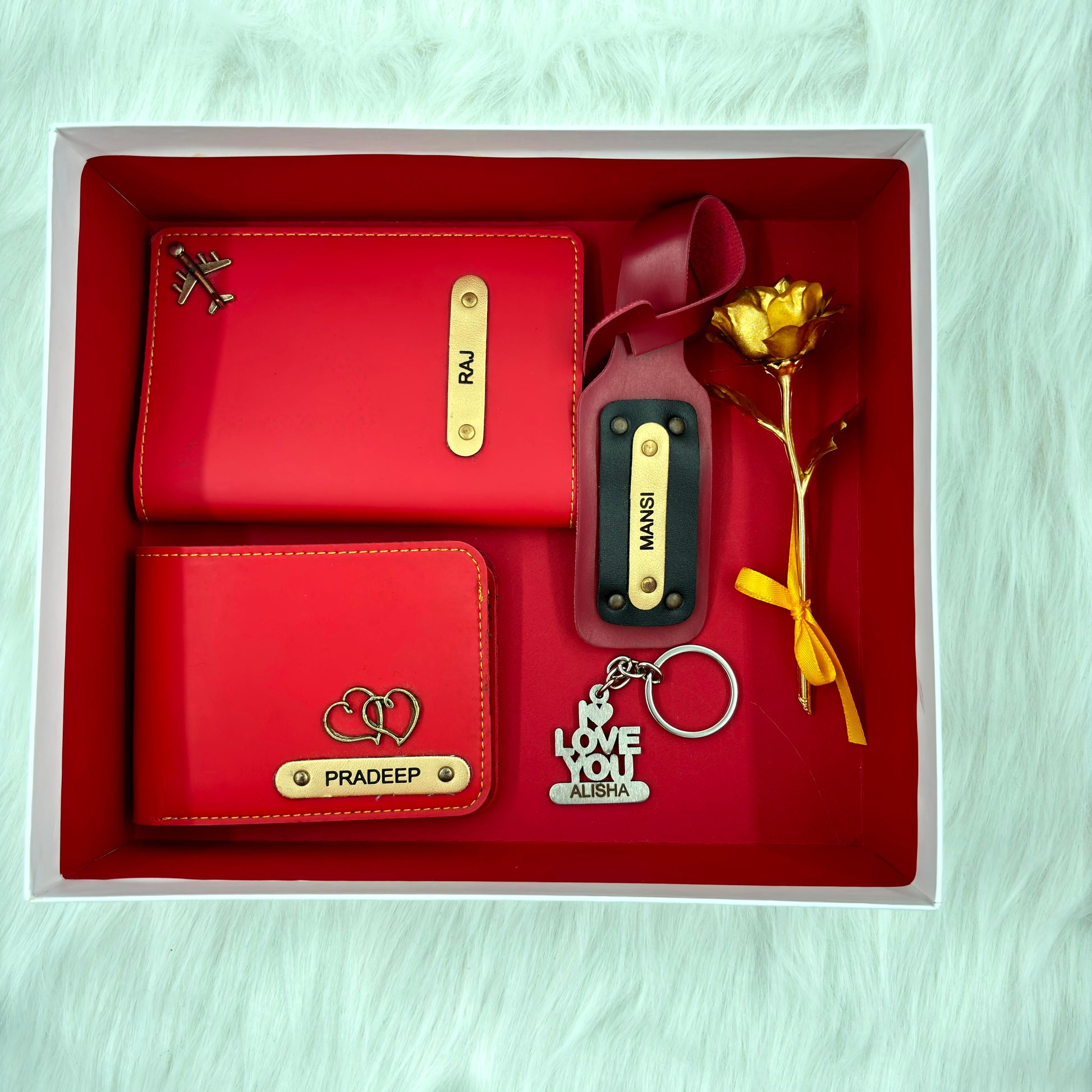 A top view of a box containing customized wine colored leather wallet, passport cover, luggage tag, I Love You keychain, and gold plated rose.