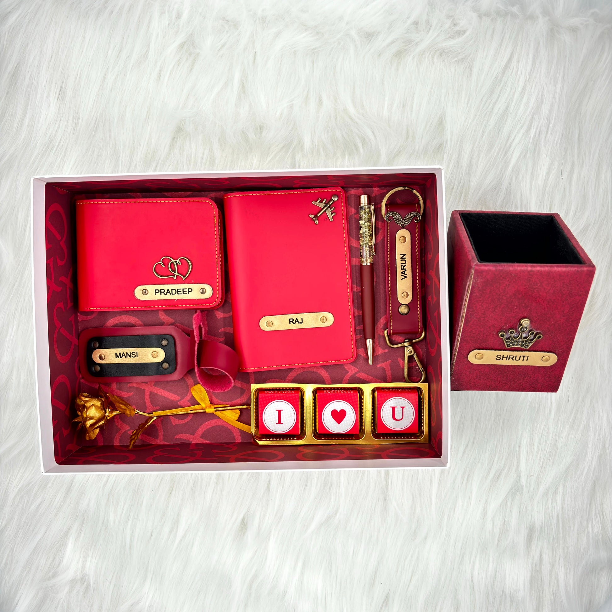 A top view of a box containing customized leather wallet, passport cover, luggage tag, I Love You chocolate, along with a gold rose, keychain and a leather box